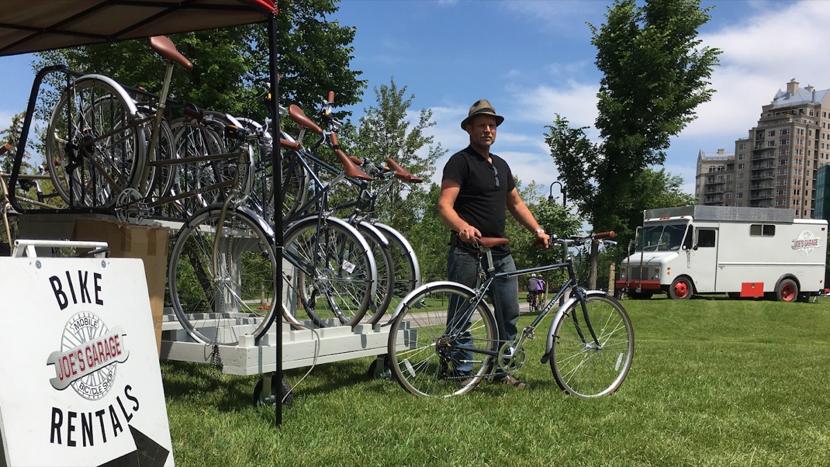 Joe standing with rental bikes on the pathway, bike rack and signage visible