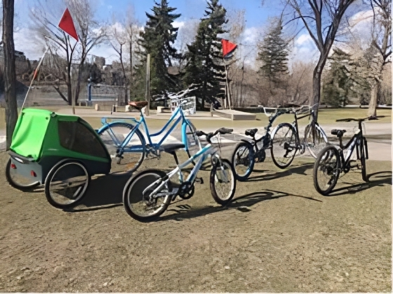 Kids' bikes, trailers, and trail-a-bikes lined up on the Bow River pathway